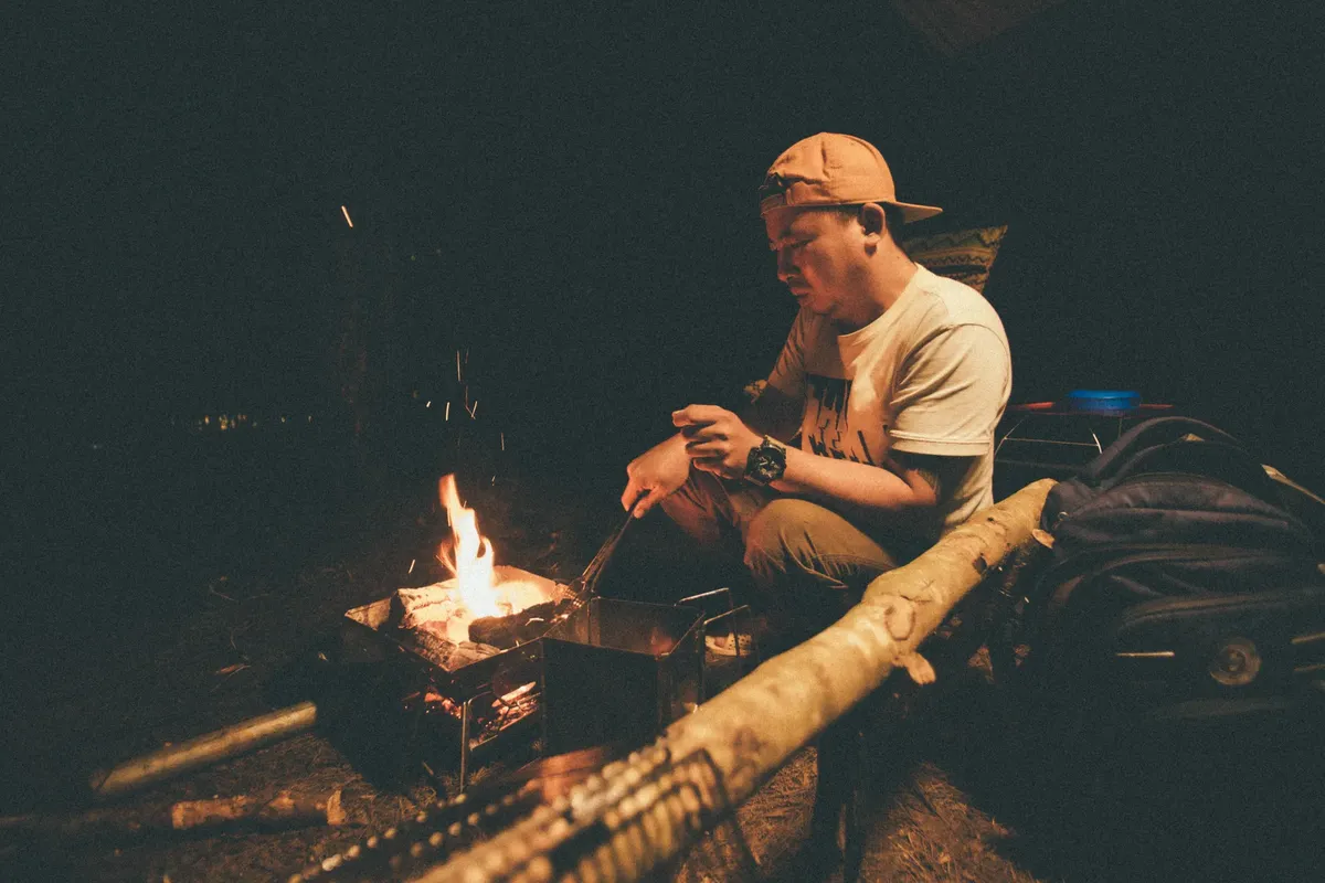 A man cooking over a campfire at night, creating a warm and rustic camping experience.