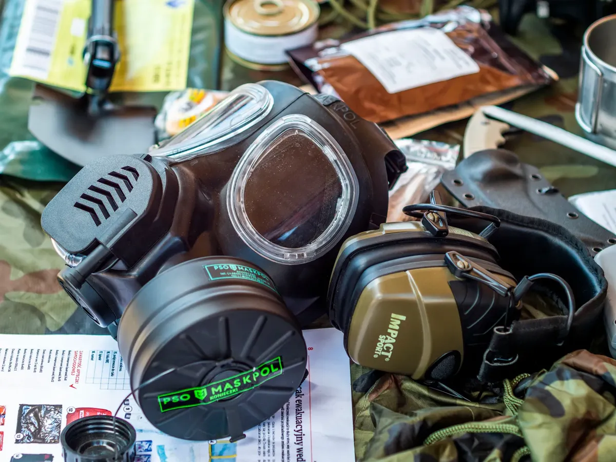 Survival gear including a gas mask and tactical headset on a camouflage background.