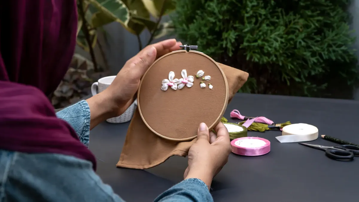 Close-up of hands working on floral embroidery in an outdoor setting.