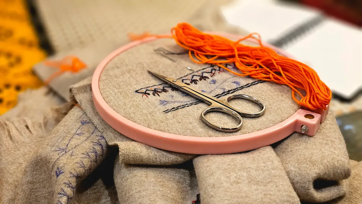 A detailed embroidery setup featuring scissors and thread in a pink hoop.
