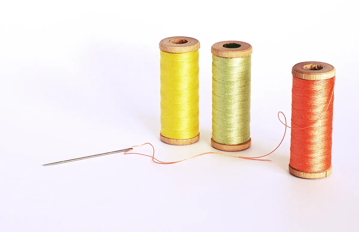 白い背景に刺繍の針が置かれた色とりどりの糸の巻き。